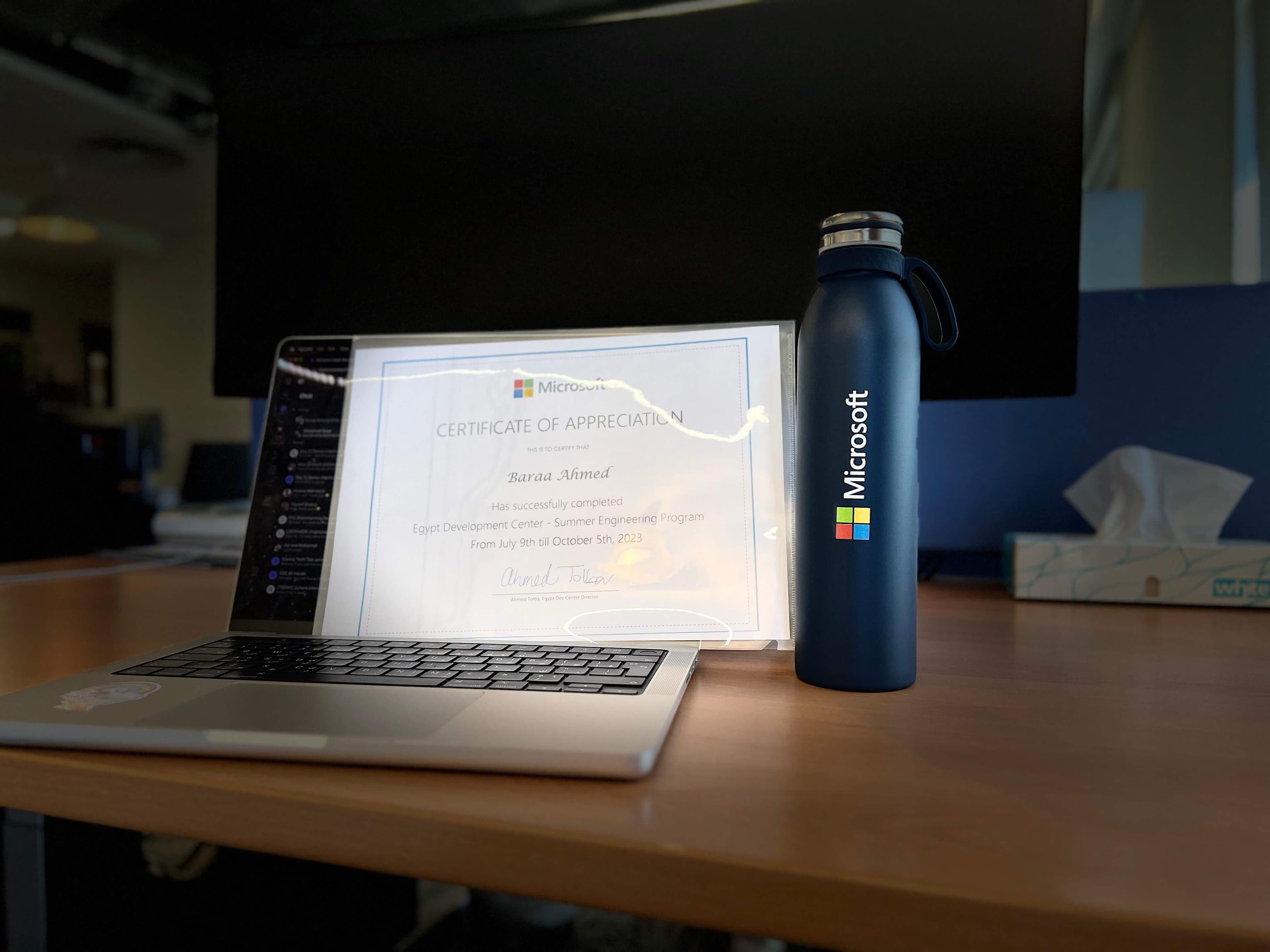 Microsoft's certificate of completion holding into a MacBook next to a Microsoft Thermal Mug